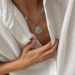 Person wearing a necklace with a green buddha jade pendant, holding a white shirt.