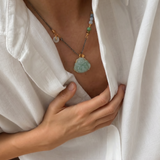 Person wearing a necklace with a green buddha jade pendant, holding a white shirt.