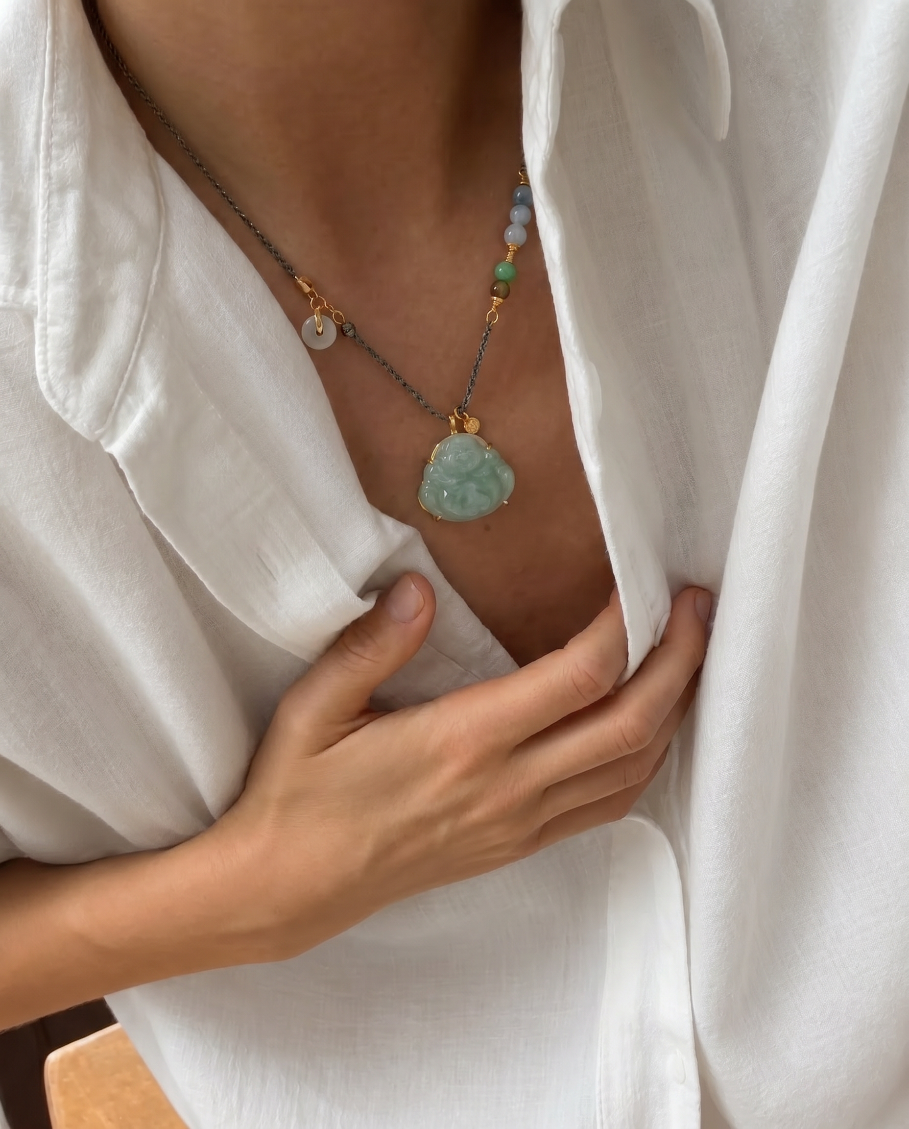 Person wearing a necklace with a green buddha jade pendant, holding a white shirt.