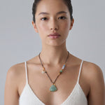 Woman wearing a necklace with a green buddha jade pendant against a plain background