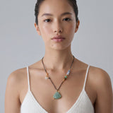 Woman wearing a necklace with a green buddha jade pendant against a plain background