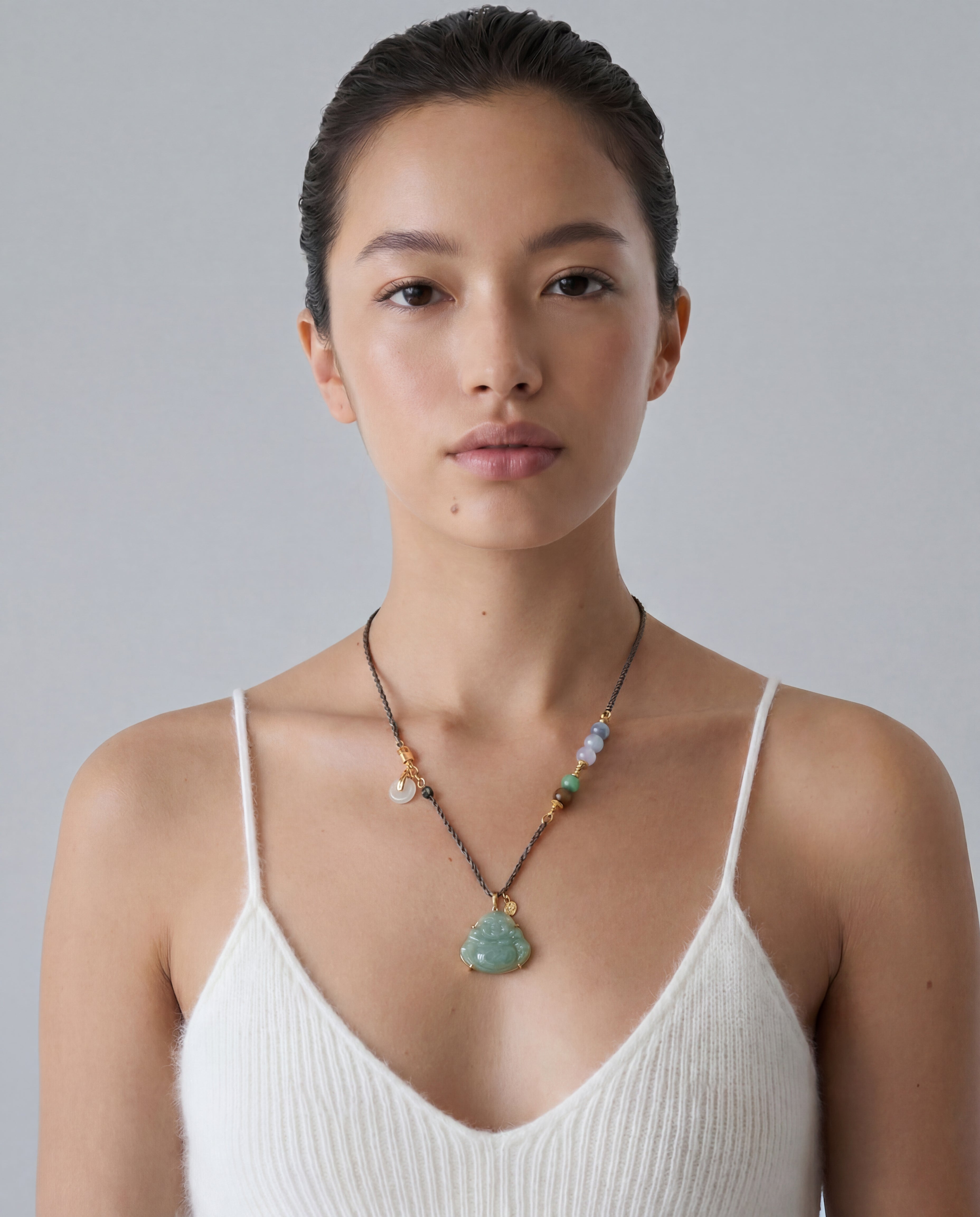 Woman wearing a necklace with a green buddha jade pendant against a plain background