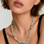 Close-up of a woman wearing a multicolored jade beaded necklace against a neutral background