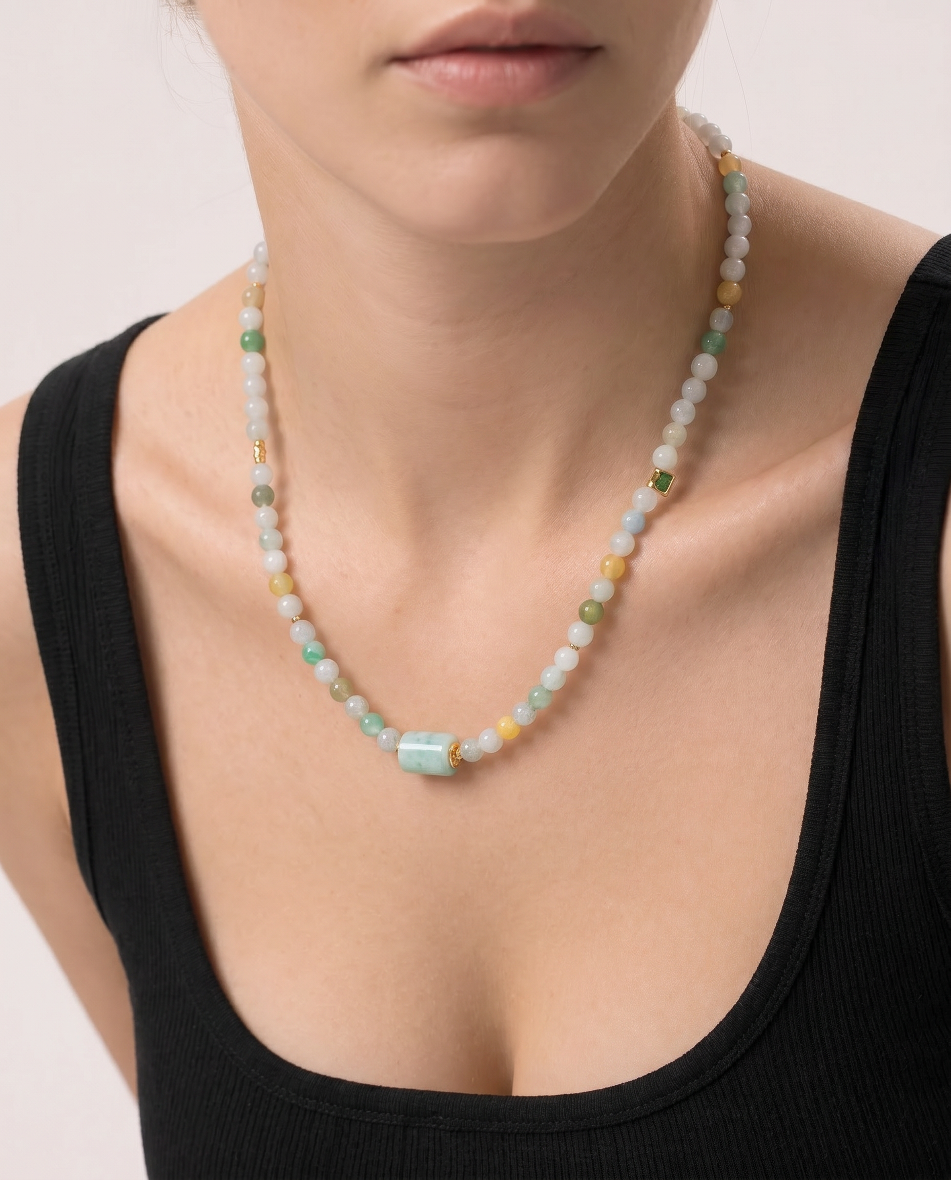 Necklace with multicolored jade beads worn by a person in a black top on a light background