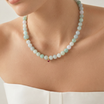 Close-up of a person wearing a white top and a jade beaded necklace