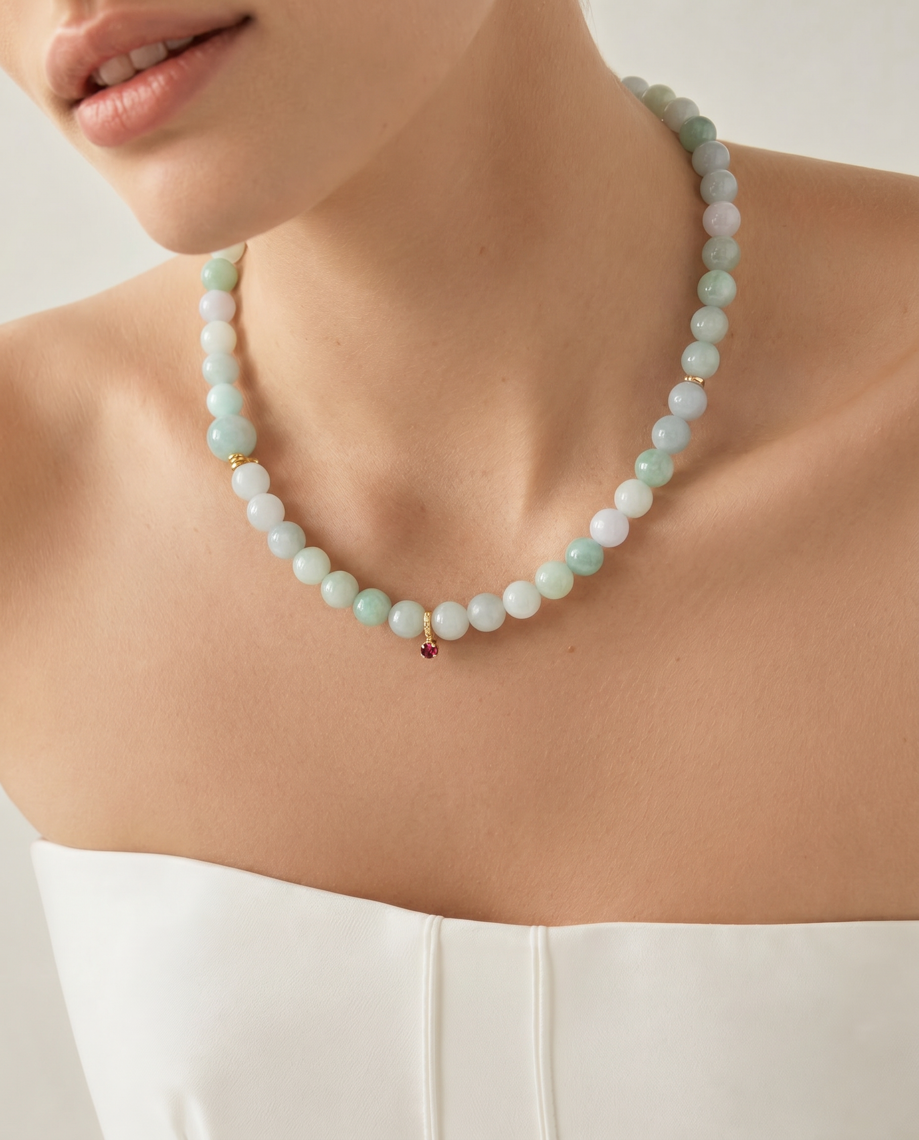 Close-up of a person wearing a white top and a jade beaded necklace