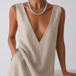 Woman wearing a beige sleeveless dress and a jade beaded necklace with a plain background