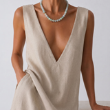 Woman wearing a beige sleeveless dress and a jade beaded necklace with a plain background