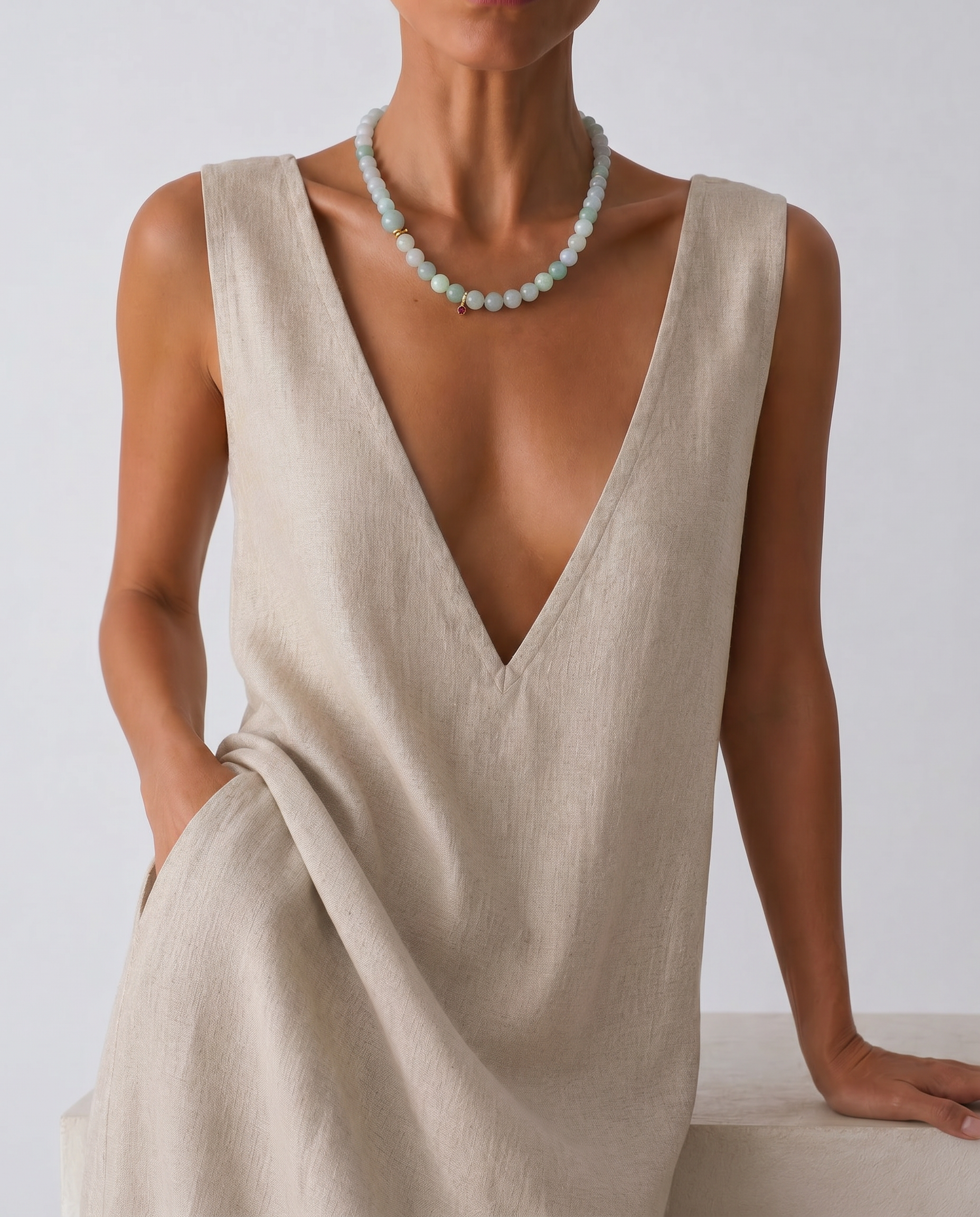 Woman wearing a beige sleeveless dress and a jade beaded necklace with a plain background