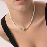 Pearl beaded necklace with a gold and green jade beads worn by a person against a neutral background