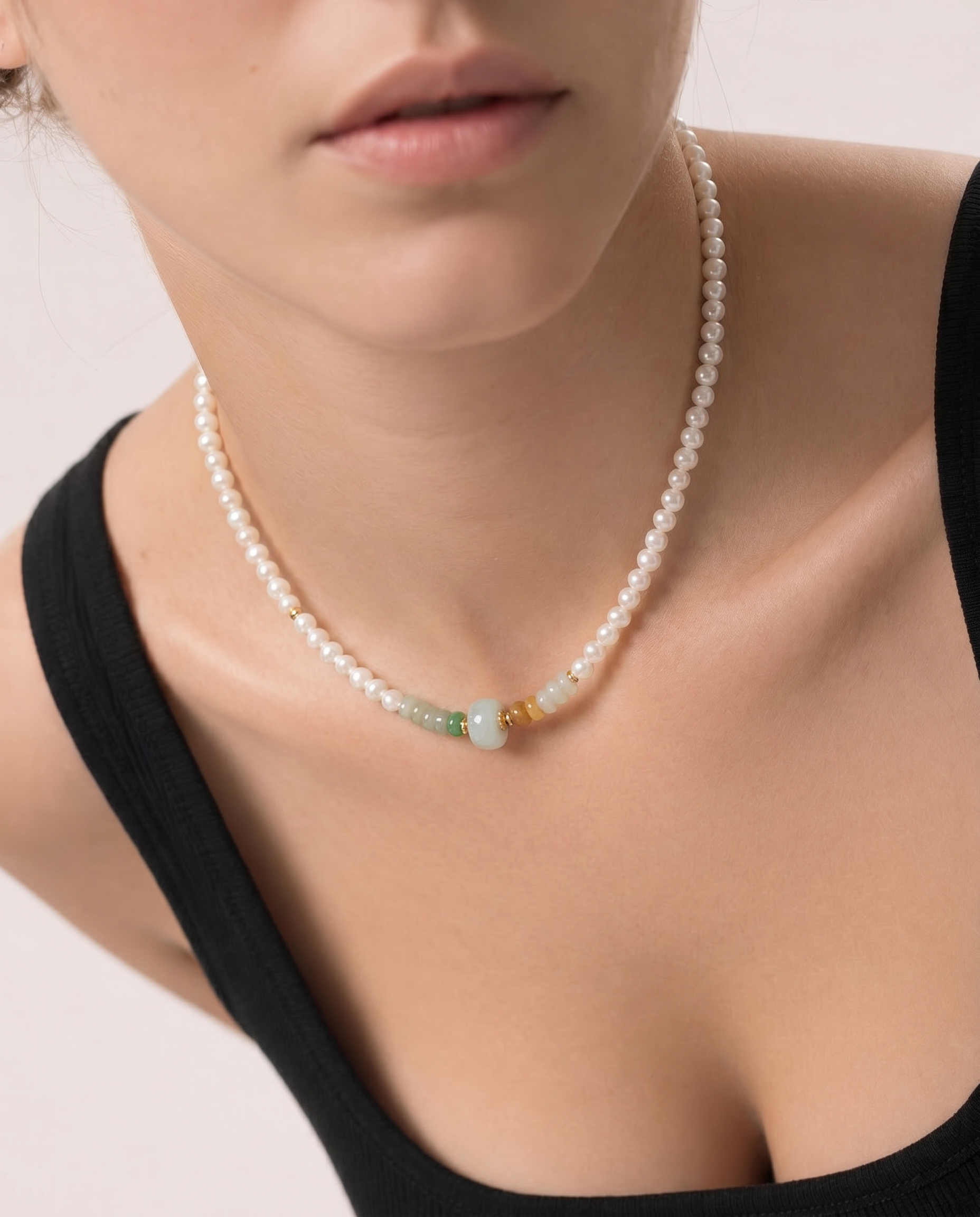 Pearl beaded necklace with a gold and green jade beads worn by a person against a neutral background