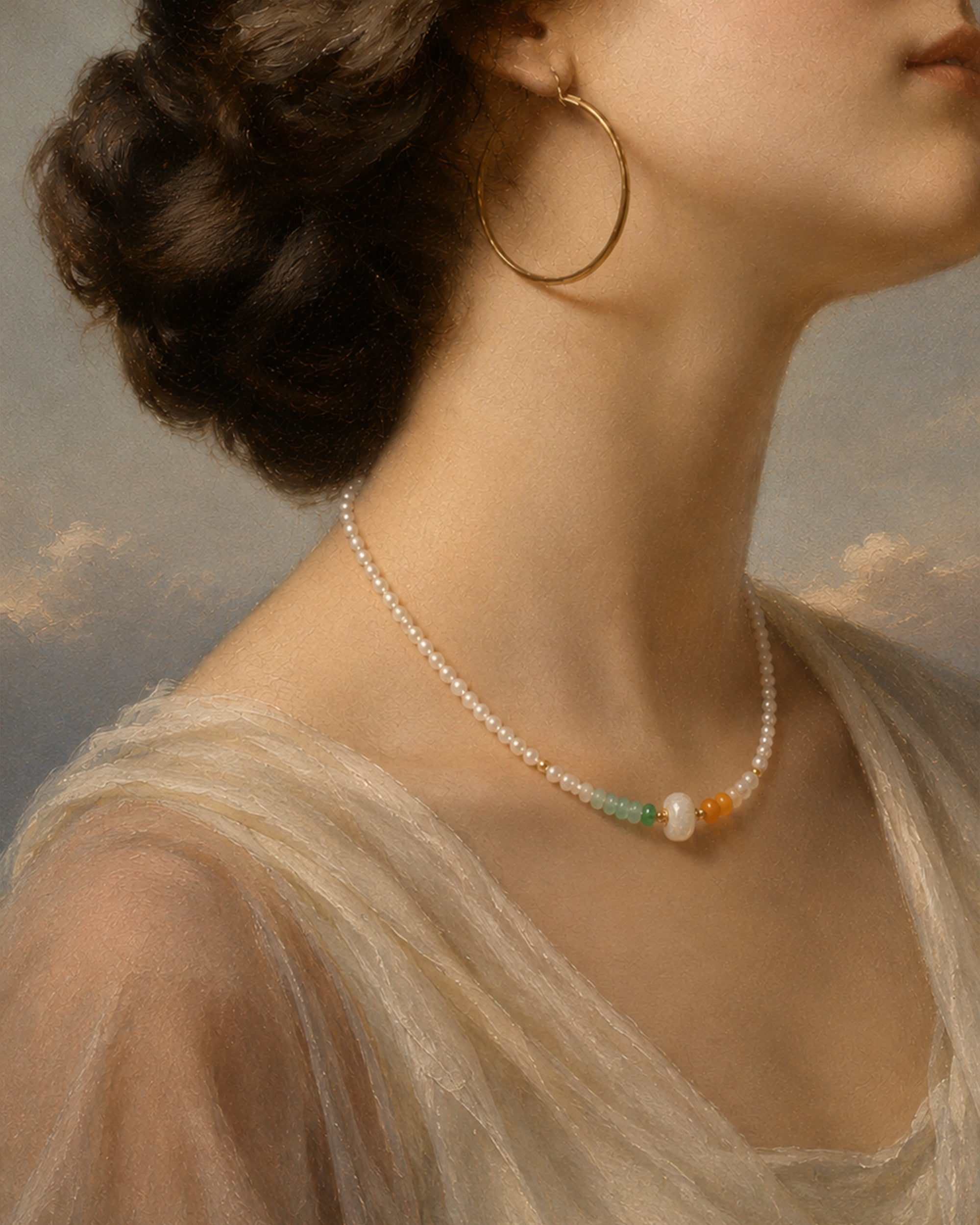 A close-up portrait of a woman wearing a delicate pearl necklace with small green, orange, and white accent beads, along with large gold hoop earrings and a sheer cream dress against a soft painted sky background.