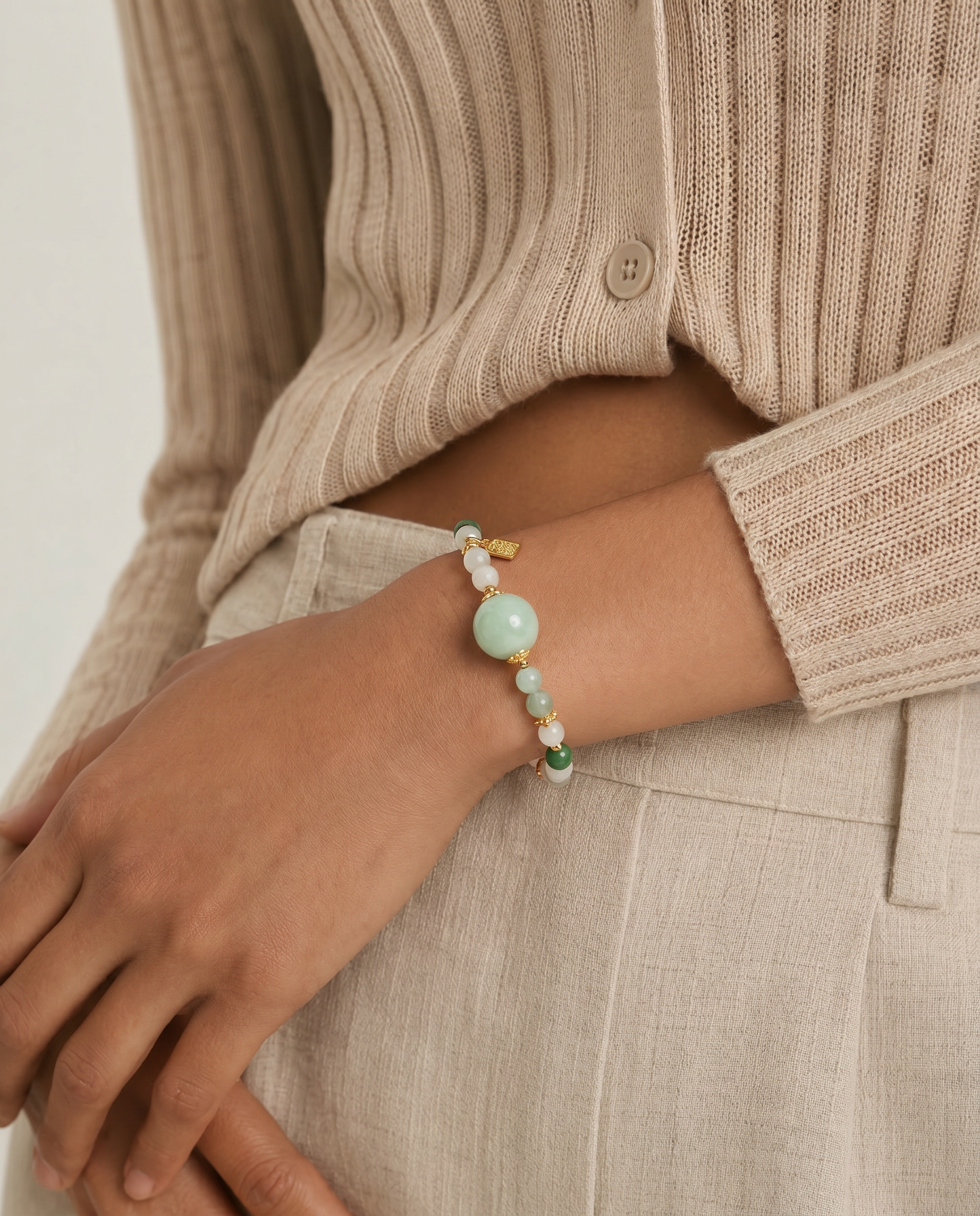 Person wearing a jade beaded bracelet on a neutral background