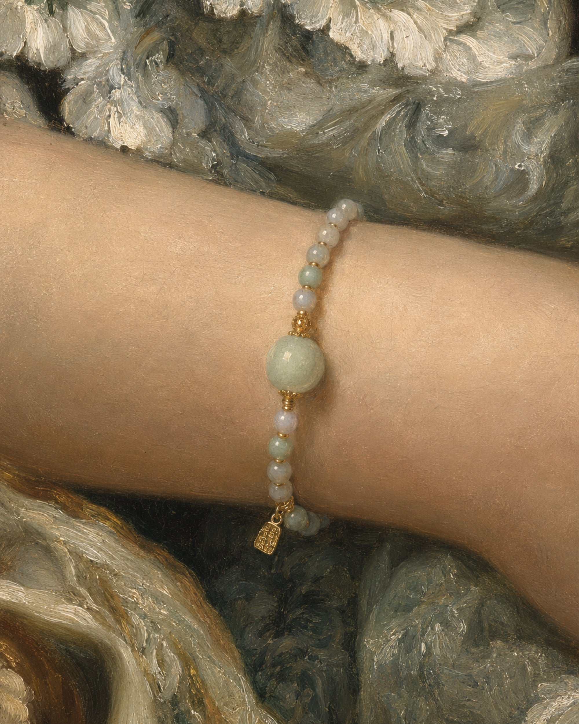 A close-up of a delicate beaded bracelet worn on a person's wrist. The bracelet features pale green and white beads with small gold spacer beads and a small gold charm, set against a painterly gray and white background.