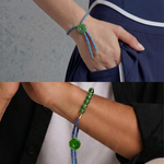 Close-up of a wrist wearing a blue cord bracelet with a green bead jade, against a neutral background.