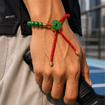 Hand wearing a red paracord bracelet with green jade beads, blurred cityscape in the background