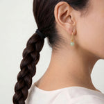 Person with braided hair wearing jade bead earring on a plain background