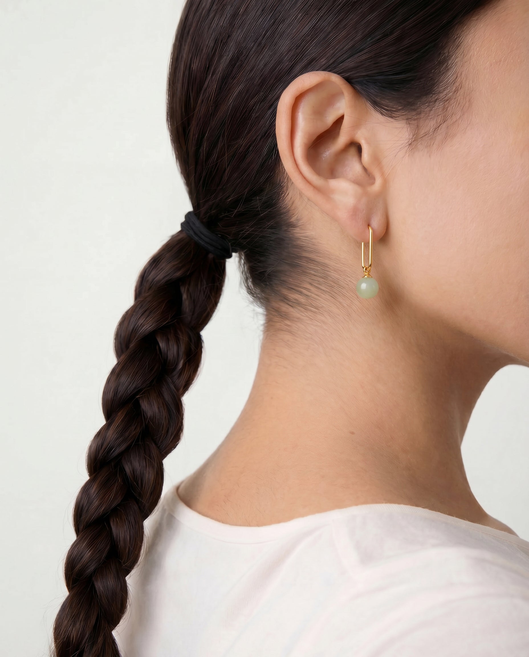 Person with braided hair wearing jade bead earring on a plain background