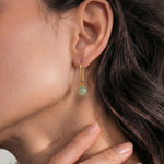 Close-up of an ear wearing a gold earring with a green jade bead, with hand holding neck