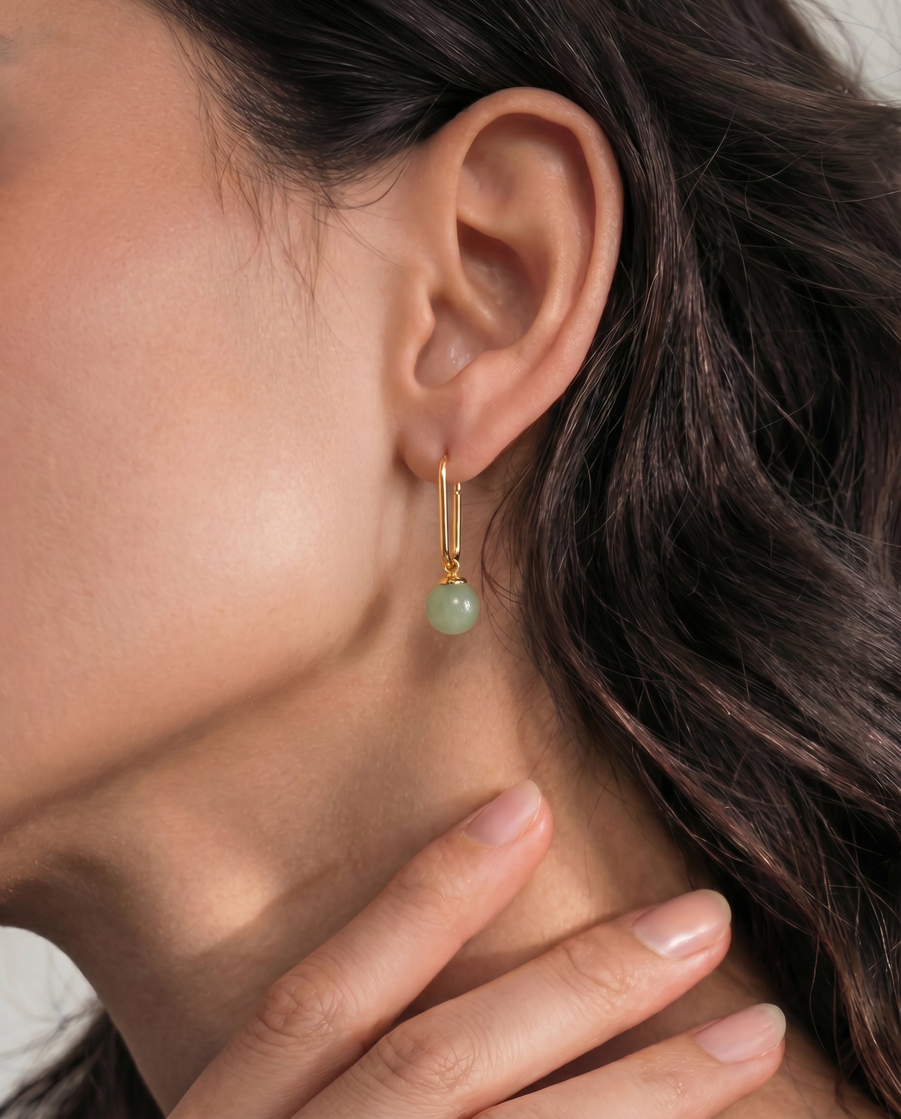 Close-up of an ear wearing a gold earring with a green jade bead, with hand holding neck