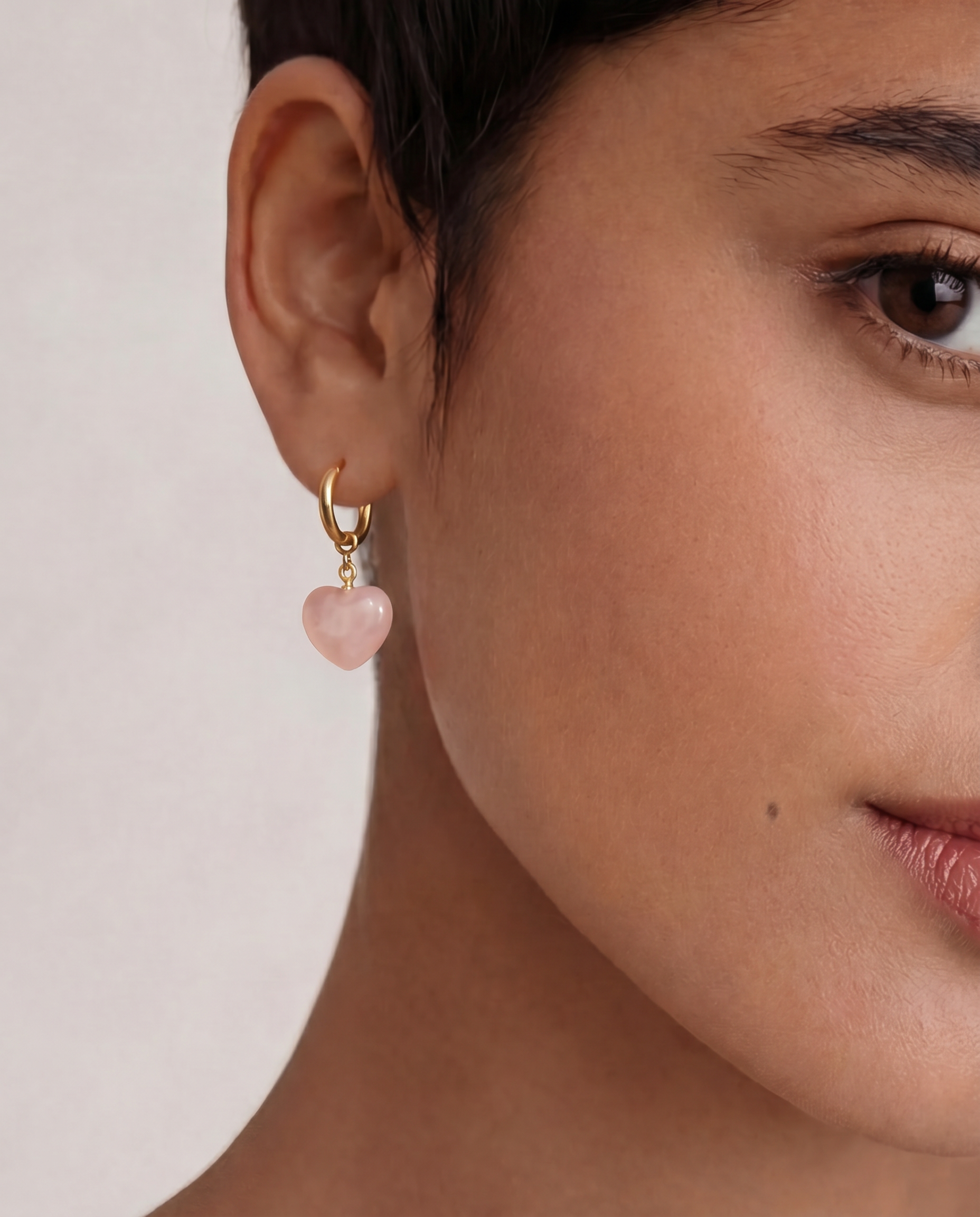 Close-up of a person wearing an earring with a pink heart-shaped charm.