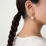 Person with braided hair wearing heart-shaped earrings on a plain background