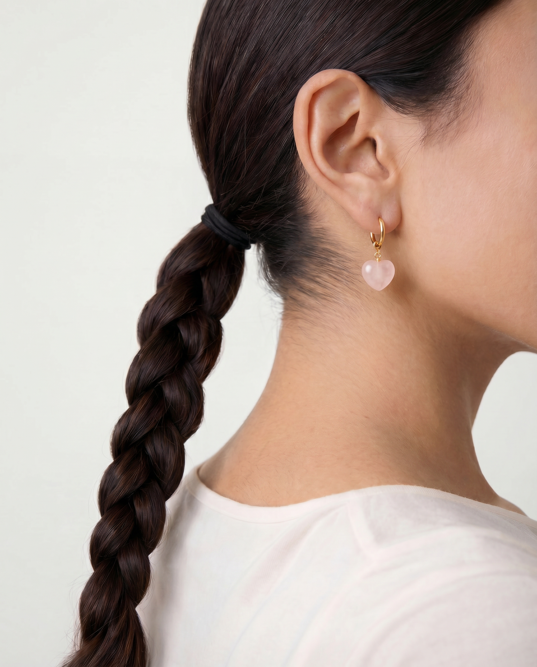 Person with braided hair wearing heart-shaped earrings on a plain background