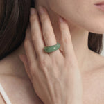 Close-up of a hand wearing a green ring with a blurred background