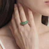 Close-up of a hand wearing a green ring with a blurred background