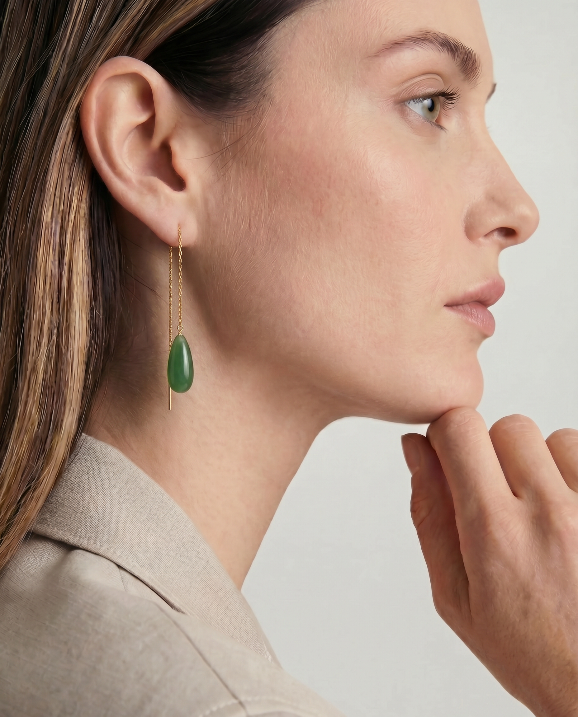 Woman wearing a green teardrop earring with a neutral background